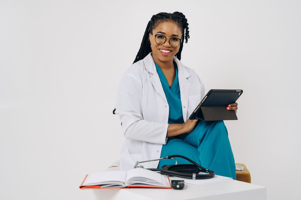 Home Smiling female doctor with a tablet and stethoscope in a bright office setting.