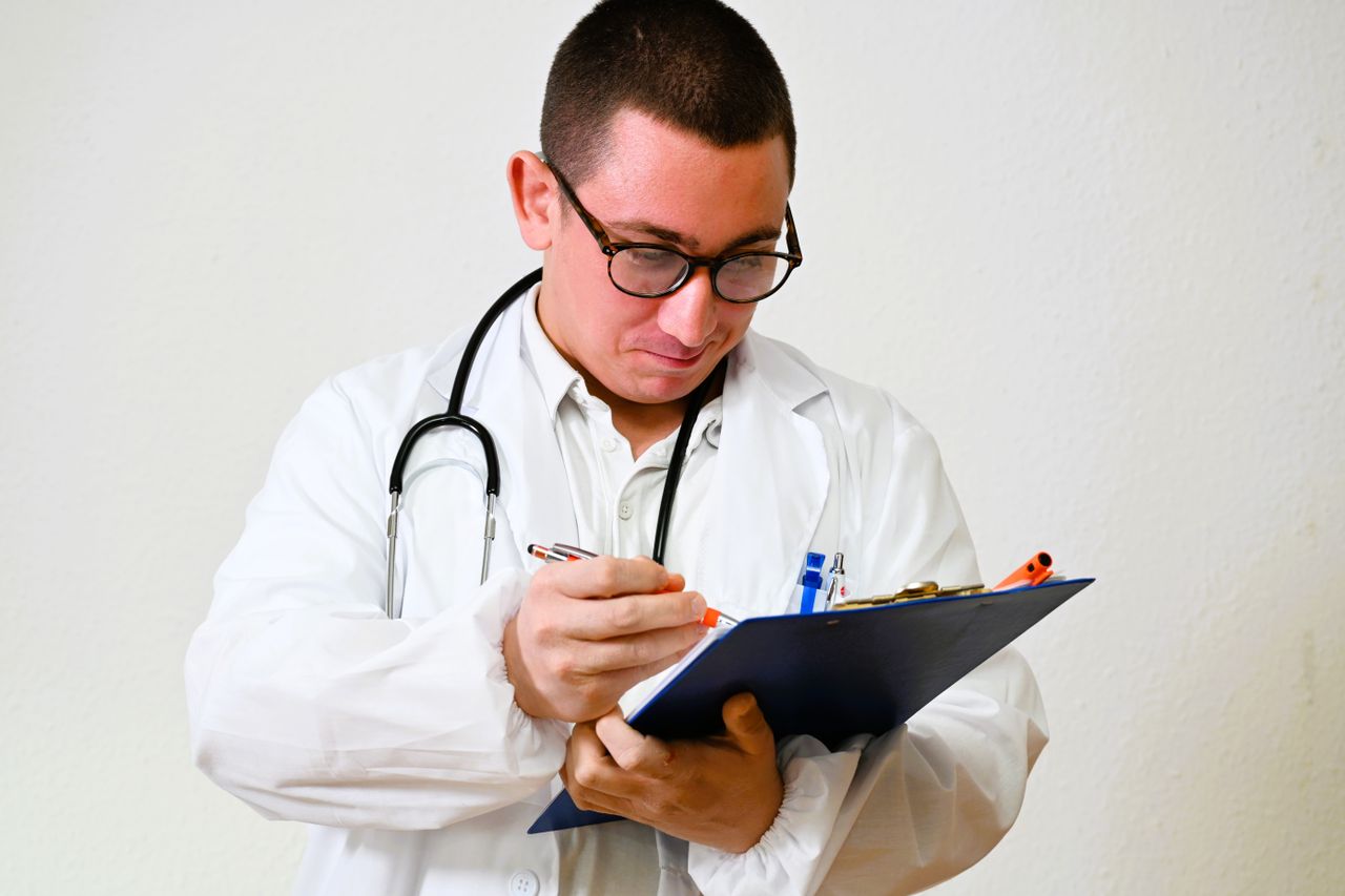 Services A male doctor in a white coat writes on a clipboard in a hospital setting, showcasing healthcare professionalism.