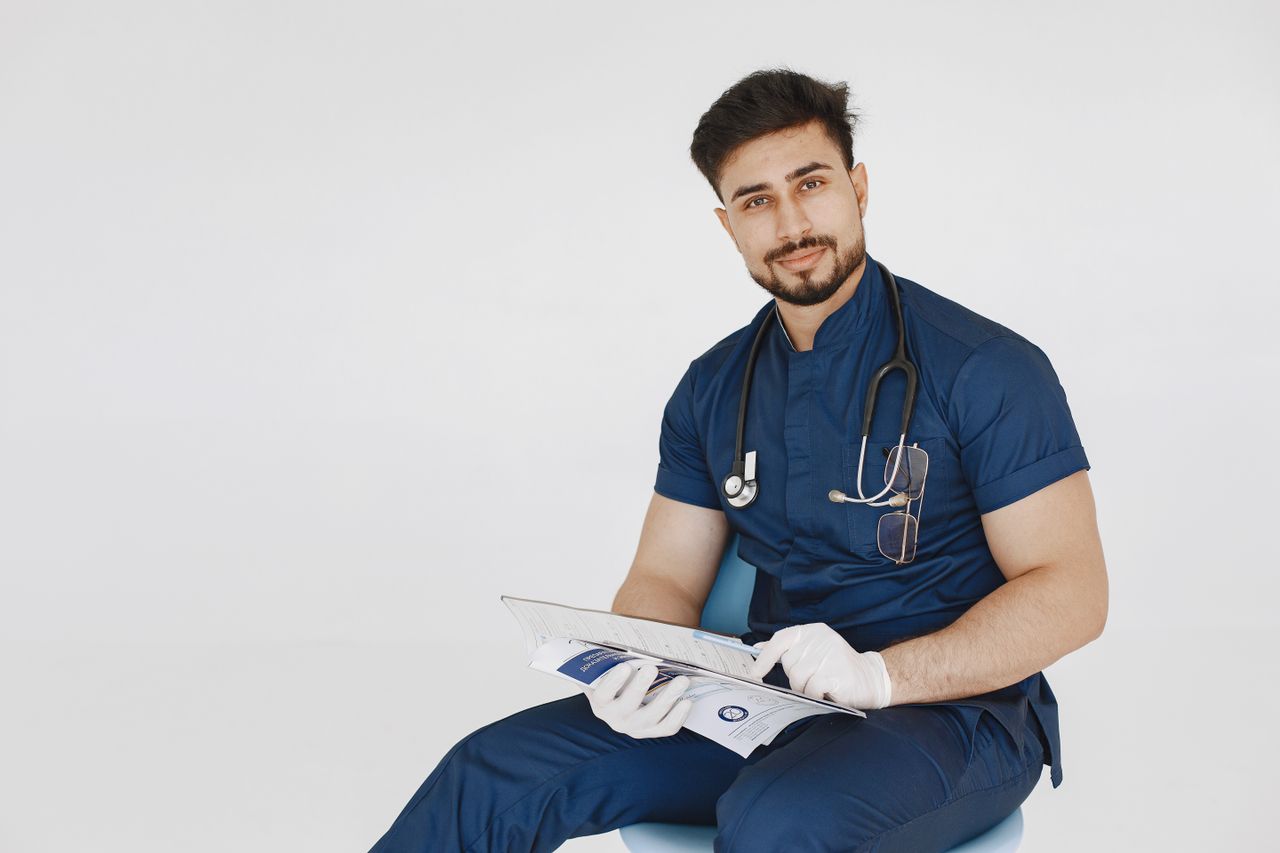 Home Young male doctor in blue scrubs reviewing medical records with a confident smile.