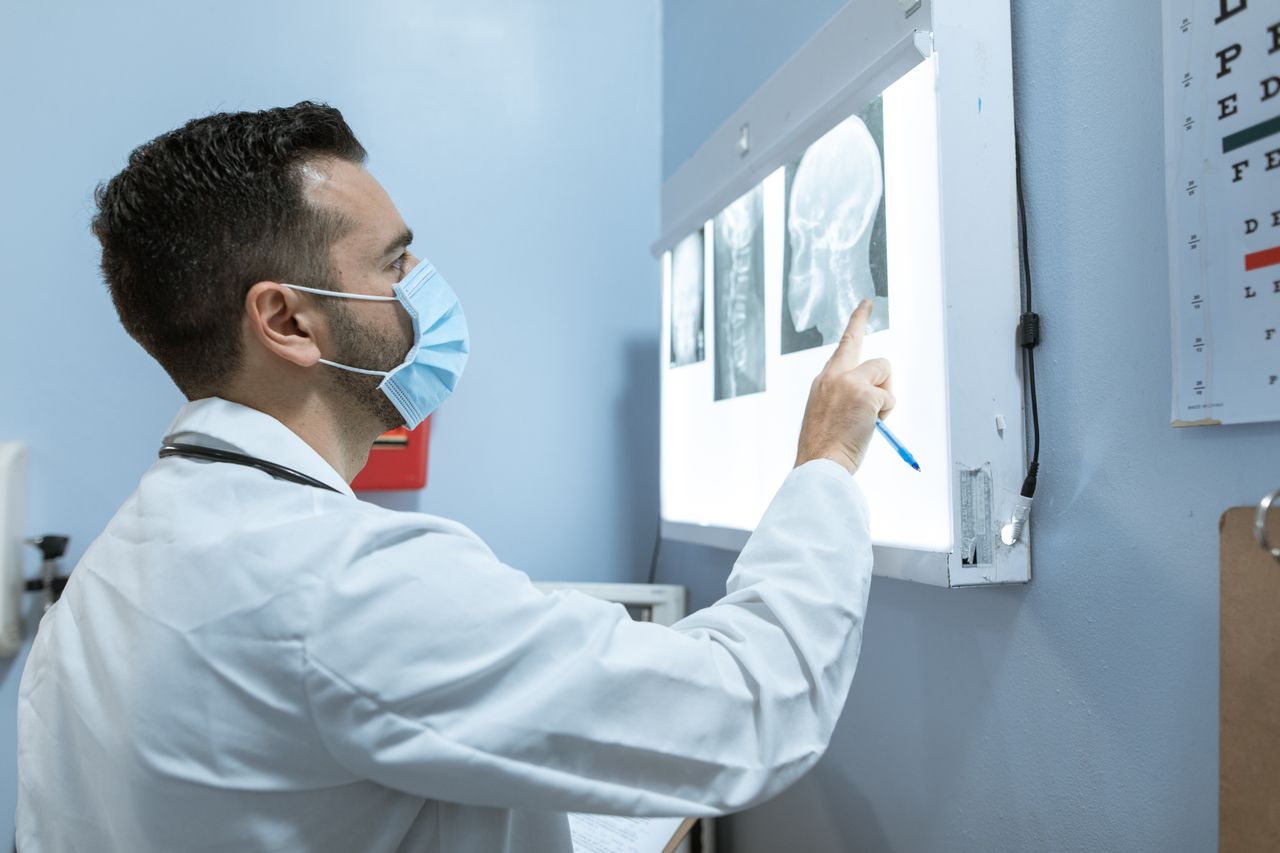 Services A healthcare professional examines brain X-rays while wearing a face mask in a hospital setting.