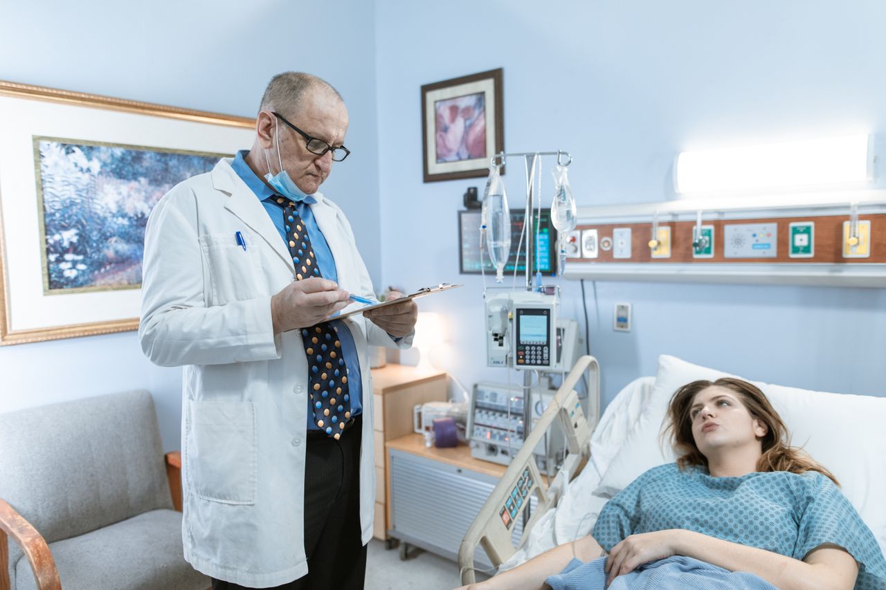Services Doctor in white coat checking patient chart in hospital room with medical equipment.