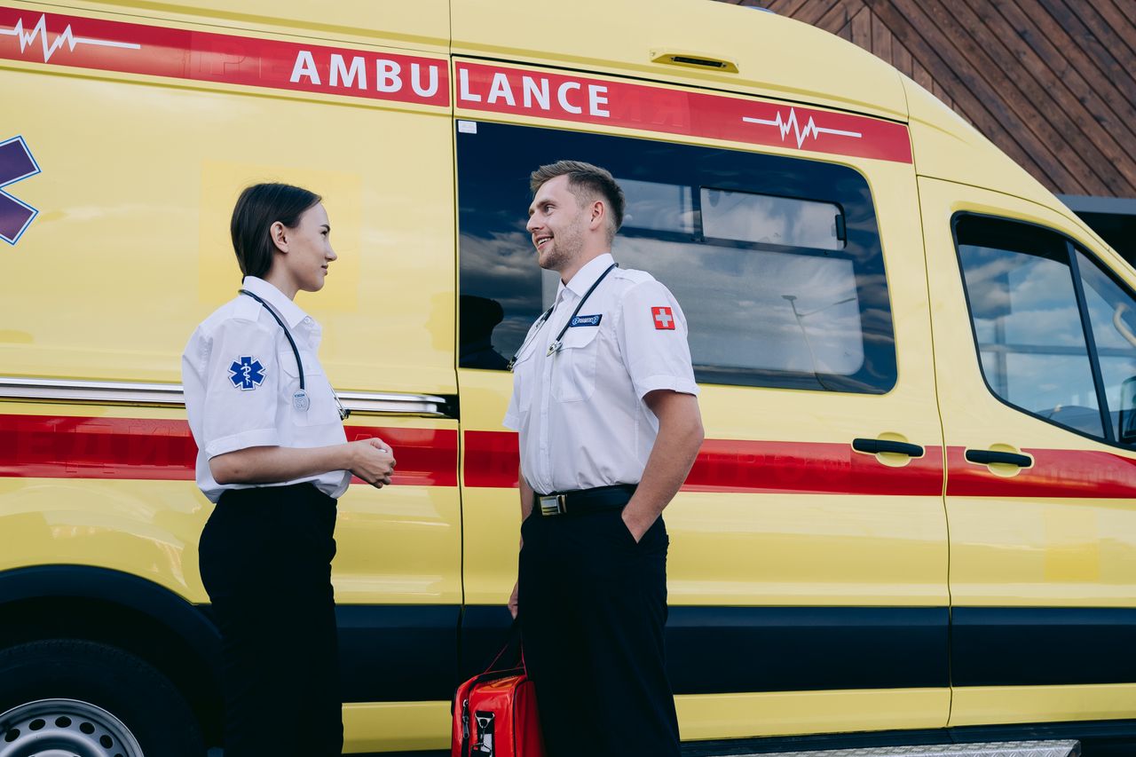 Home Two paramedics talking beside a bright yellow ambulance, showcasing teamwork and medical readiness.